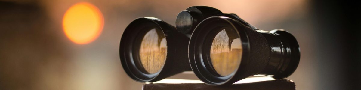 Close-up view of binoculars on a surface with sunset reflection in lenses.